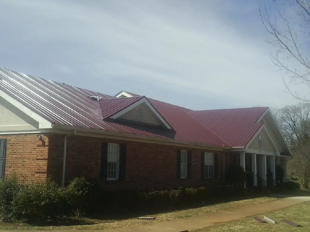 Red metal roof with gabled entries on a long brick building, from a Hail Damage Roof Repair job in Blythe