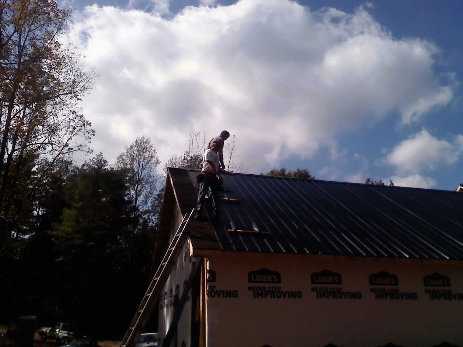 Roofer fastening dark metal panels high against a cloudy sky, from a Roof Inspection job in Blythe