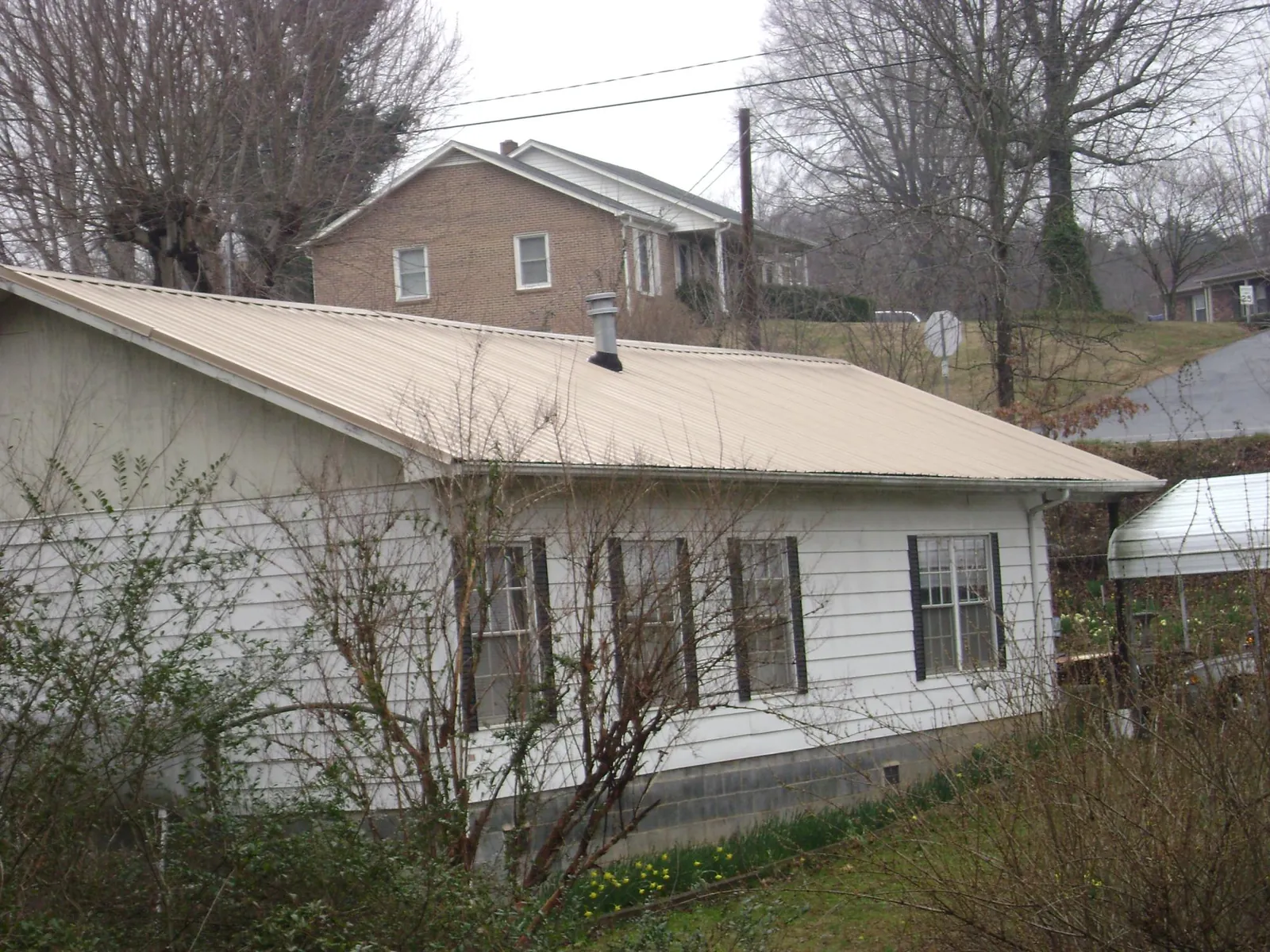 Tan metal roof on a white sided house set into a hillside — Commercial Roofing by Roofing Brothers in Blythe