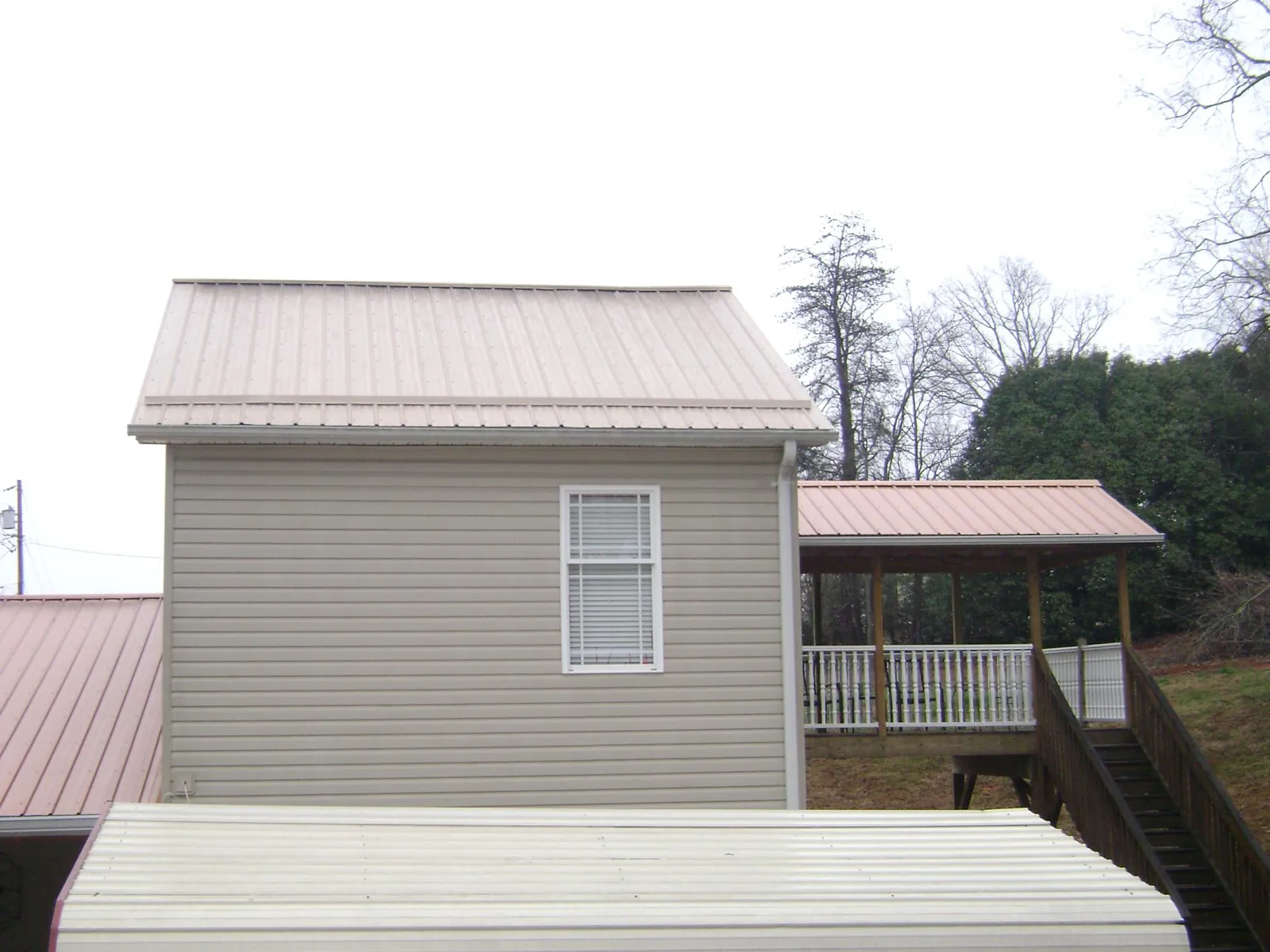 Tan metal roofs on a two story addition and attached porch, from a Roof Replacement job in Blythe